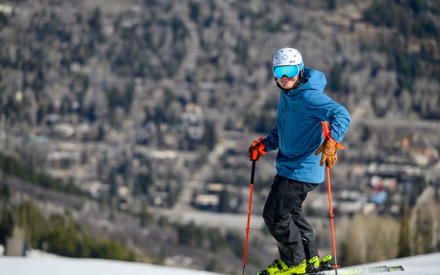 Tomas Mical standing on skis, smiling, with the town of Aspen in the valley behind him